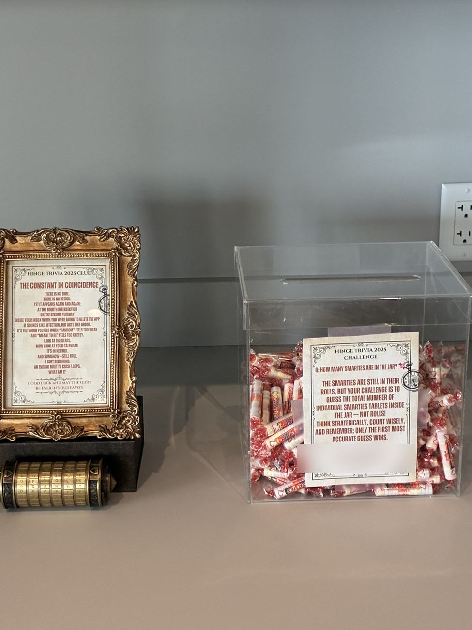 A clear ballot box full of Smarties rolls beside the framed clue and a small brass cryptex