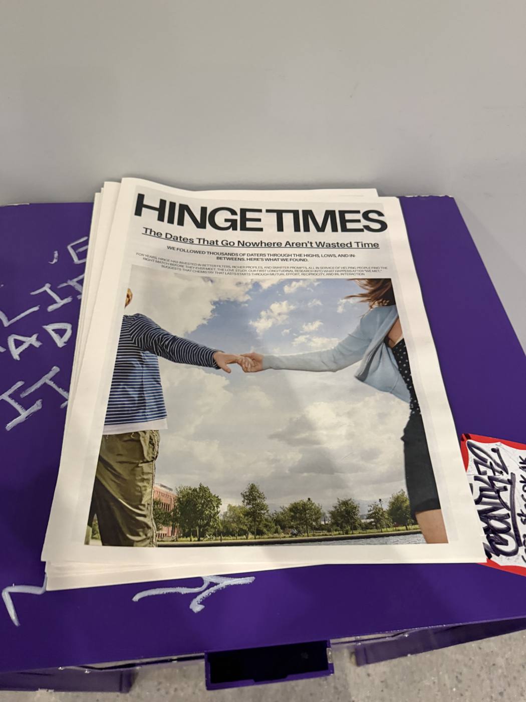 A purple Hinge Times newsstand stacked with newspapers